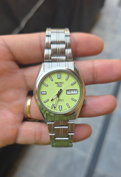 Seiko 5 automatic men's watch with a bright, full-lume yellow-green dial and stainless steel bracelet.